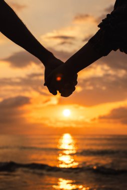 Gün doğumunda el ele tutuşan çiftlerin romantik anları, sakin deniz dalgaları ve altın gökyüzüne yansıyan ılık güneş ışığı. Yüksek kalite fotoğraf