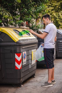 Günlük giysiler içindeki bir adam, Roma 'da bir caddede plastik şişeleri sarı bir geri dönüşüm kutusuna dönüştürüyor ve atıkların ayrılmasından ve çevresel farkındalıktan sorumlu hale getiriyor. Yüksek kalite fotoğraf