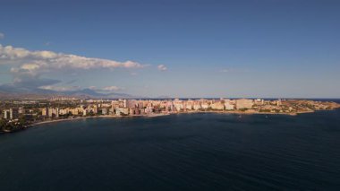 Akdeniz kıyısı boyunca uzanan Alicante şehrinin hava manzarası ve açık bir akşam gökyüzünün altında dağlar. Yüksek kalite 4k görüntü