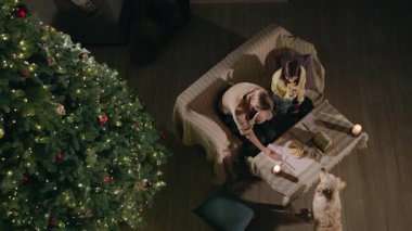 İki çocuğun Noel ağacının yanında oturup mumların yanında kurabiye çizip süslediği ve rahat bir tatil ortamında Golden Retriever oynadığı en iyi manzara. Yüksek kalite 4k görüntü