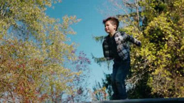 Neşeli küçük çocuk güneşli bir günde trambolinde atlıyor, eğleniyor ve aktif oyun zamanının tadını çıkarıyor. Yüksek kalite 4k görüntü