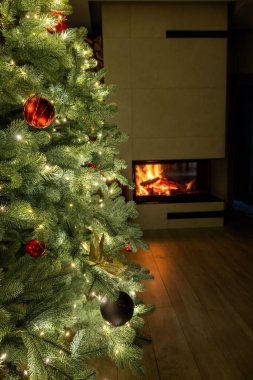 Parlayan ışıkları ve sıcacık bir şöminenin yanında duran kırmızı süslemeleri olan güzel bir Noel ağacı neşeli ve sıcak bir tatil atmosferi yaratıyor. Yüksek kalite fotoğraf