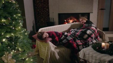 İki genç kız, Noel ağacının yanındaki ekose bir battaniyenin altında, sıcak tatil ışıkları ve rahat dekorasyonlarla çevrili, parıldayan bir şöminede huzur içinde uyuyorlar. Yüksek kalite