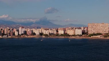 Alicante 'nin modern konut binaları, kumlu plajları ve Akdeniz' de arka planda dağlarla birlikte yelkenli tekneleri olan kıyı manzarası. Yüksek kalite 4k görüntü