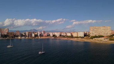 Gün batımında sakin Akdeniz 'de Alicante sahili, binalar, kumlu sahil manzarası ve yelkenli tekneleri. Yüksek kalite 4k görüntü