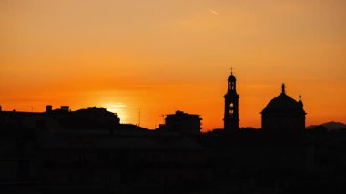 Bergamo, İtalya 'da gün batımının zamanı. Güneş şehrin silueti ve sıcak turuncu gece ışığında kilise kulelerinin arkasından yavaşça iniyor. Yüksek kalite 4k görüntü