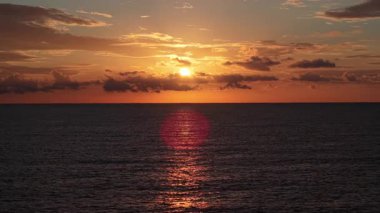 İspanya 'nın Altea kenti yakınlarındaki sakin Akdeniz' in üzerinde parlak bir gün doğumu, suya yansıyan altın güneş ışığı ve sıcak tonlarda parlayan dağınık bulutlar. Yüksek kalite 4k görüntü