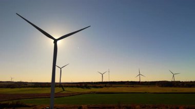 Rüzgar türbinleri gün batımında yeşil alanlar üzerinde dönüyor, temiz bir gökyüzüne karşı temiz enerji üretiyorlar. Yüksek kalite 4k görüntü