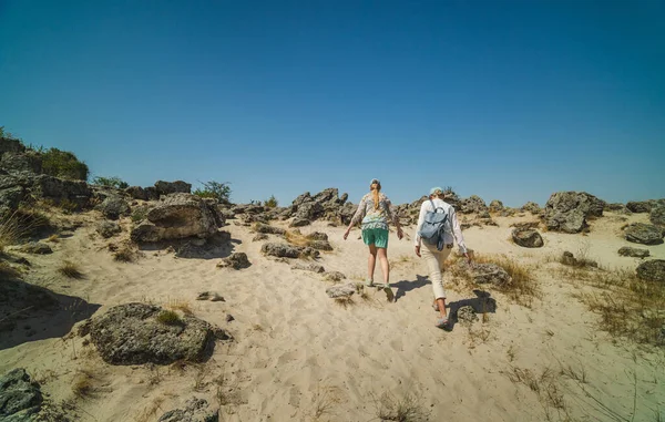 Bulgaristan 'ın Pobiti Kamani kentindeki kumlu ve kayalık arazide açık mavi bir yaz gökyüzü altında yürüyüş yapan iki kadın. Yüksek kalite fotoğraf