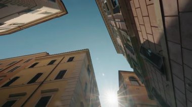 Güneş ışığı, dar bir Roma caddesindeki renkli tarihi binalar arasında parlıyor.. 