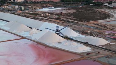 İspanya 'da gün batımında pembe tuz gölleri yakınlarındaki bir tuz işleme tesisinde büyük beyaz tuz yığınları ve endüstriyel taşıyıcı sistemin havadan görüntüsü. Yüksek kalite 4k görüntü