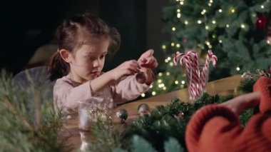 Evde Noel süsleri süsleyen küçük bir kız. Masada şenlikli ışıklar ve baston şekerlerle. Yüksek kalite 4k görüntü