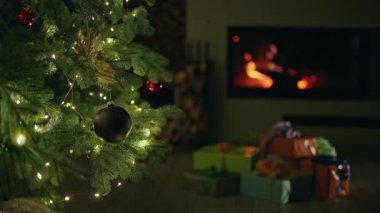 Süslü bir ağacın altında, şöminenin yanında parlayan ışıklarla Noel hediyeleri, evde şenlikli ve rahat bir tatil ortamı yaratıyor. Yüksek kalite 4k görüntü