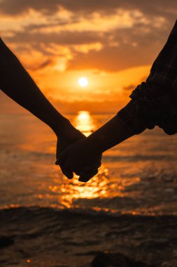 Gün doğumunda plajda el ele tutuşan çiftlerin silueti sakin denizi yansıtan altın güneş ışığıyla. Yüksek kalite fotoğraf