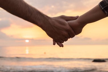 Denizin üzerinde güzel bir gün doğumuna karşı el ele tutuşan iki insanın yakınlaşması sevgi, birlik ve sakin bir sahil atmosferine olan güveni sembolize ediyor. Yüksek kalite fotoğraf