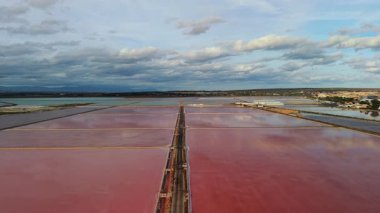 İspanya 'nın Santa Pola kenti yakınlarındaki canlı pembe ve turkuaz tuz göletlerinin hava manzarası, öğleden sonra ışığı altında dramatik bulutlar ve yansımalar. Yüksek kalite 4k görüntü