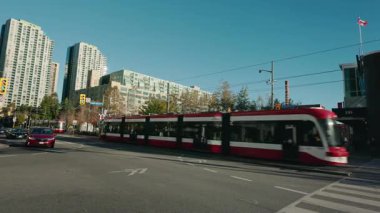 Toronto, Kanada, 28 Ekim 2025: Yoğun bir Toronto kavşağında süzülen kırmızı modern tramvay şehir binaları ve trafik arasında toplu taşımayı vurguluyor. Yüksek kalite 4k görüntü