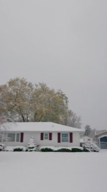 Garaj yolu olan tipik bir Amerikan mahallesinde, karlı bir banliyö caddesi, park edilmiş bir SUV ve çatıları kaplayan taze kar ve araba penceresinden görünen sonbahar ağaçları. Yüksek kalite 4k görüntü