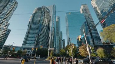 Toronto, Kanada, 28 Ekim 2025: Toronto şehir merkezinde modern cam gökdelenler ve yoğun şehir trafiğiyle çevrili güneşli bir kavşaktan geçen yayalar. Yüksek kalite 4k görüntü