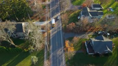 Tipik küçük bir Amerikan kasabasında banliyö caddesi boyunca giden sarı bir okul otobüsünün hava görüntüsü. Yüksek kalite 4k görüntü