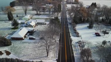 Soğuk bir kış gününde evleri, ağaçları ve düz bir yolu olan karlı bir Amerikan banliyö mahallesinin havadan görünüşü. Yüksek kalite 4k görüntü