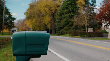 Bir kadın yol kenarındaki posta kutusuna doğru yürüyor, mektupları içine yerleştiriyor, kırmızı bayrağı göndere çekiyor ve bir sonbahar günü sakin bir banliyö caddesi boyunca ayrılıyor. Yüksek kalite 4k görüntü