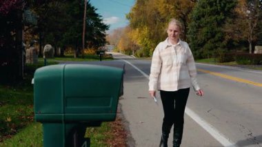 Elinde bir mektupla banliyö yolunda yürüyen bir kadın, açık bir sonbahar gününde posta göndermeye hazırlanıyor. Yüksek kalite 4k görüntü