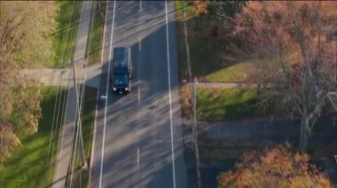 Wilson, New York, 20 Ekim 2025: Sonbahar ağaçlarıyla dolu bir banliyö yolunda giden Amazon dağıtım aracının hava görüntüsü. Yüksek kalite 4k görüntü