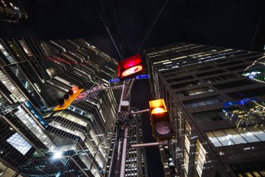 Yüksek cam gökdelenlerle çevrili şehir kanyonunun merkezinde parlayan kırmızı bir trafik ışığı duruyor. Yüksek kalite fotoğraf