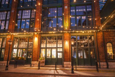 Toronto 'daki tarihi Damıtma Bölgesi' nin akşam manzarası aydınlanmış tuğla mimarisi, uzun pencereler ve şenlikli sicim ışıkları. Yüksek kalite fotoğraf