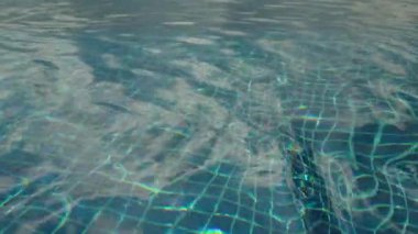 Güneş ışığı dalgalanmaları ve yansımaları olan temiz yüzme havuzunun soyut görüntüsü yüzeyin altında görülen mavi karo deseni, arka plan dokusunun asgari düzeyde durması. Yüksek kalite 4k görüntü