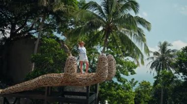 Orta yaşlı bir kadın, Koh Samui 'de palmiye ağaçlarıyla çevrili, el şeklinde bir perspektif platformunda duruyor. Yüksek kalite 4k görüntü