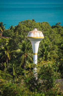 Turkuvaz denizi ve berrak gökyüzü ile yoğun tropik palmiye ormanlarının üzerinde yükselen su kulesi, yemyeşil ve kıyı manzaralarıyla çevrili ada altyapısı. Yüksek kalite fotoğraf