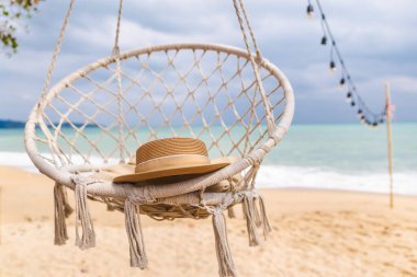 Hasır şapka, kumlu tropikal plajın üzerinde asılı, turkuaz okyanus ve sicim ışıkları, huzurlu deniz kenarı rahatlama sahnesi. Yüksek kalite fotoğraf