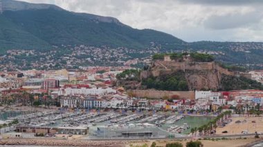 Denia Marina 'nın havadan görünüşü ve kayalık tepedeki tarihi şato. Arkasında Akdeniz şehir manzarası ve dağlar var. Yüksek kalite 4k görüntü