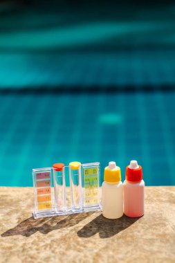 PH ve klor dereceli havuz suyu test kiti ve taştan havuz kenarındaki şişeleri ayırmak, yüzme havuzu bakımı ve mavi arka planlı su kalite kontrol konsepti. Yüksek kalite fotoğraf