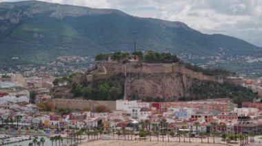 İspanya 'da yeşil dağ zeminli, renkli şehir merkezi, marina ve Akdeniz kıyı şeridinin üzerindeki Kayalık Tepe üzerindeki Denia tarihi kalesinin havadan görünüşü. Yüksek kalite 4k görüntü