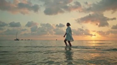 Günbatımında çıplak ayakla sığ denizde yürüyen genç kadın ve Lipa Noi sahilinde gün doğumu, Koh Samui, yelkenliyle tropik seyahat sahnesi. Yüksek kalite 4k görüntü