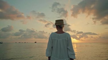 Günbatımında ve Lipa Noi plajında gün doğumunda çıplak ayakla sığ denizde duran genç kadın, Koh Samui, dramatik gökyüzü ve sakin su ile tropik seyahat sahnesi. Yüksek kalite 4k görüntü