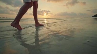 Gün batımında Lipa Noi plajında çıplak ayakla sığ denizde yürüyen genç bir kadın, Koh Samui, altın yansıması ve geniş kopya uzayı ile huzurlu bir tropikal seyahat anı. Yüksek kalite 4k görüntü