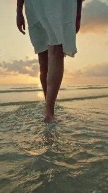 Gün batımında ve Lipa Noi plajında gün doğumunda çıplak ayakla yürüyen genç bir kadın, Koh Samui, altın yansımalı huzurlu bir tropikal seyahat anı. Yüksek kalite 4k görüntü