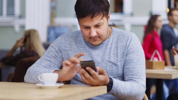 Homem trabalha com telefone, smartphone, gadget no café, sorrindo — Vídeo de Stock