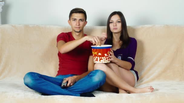 Молодая пара смотрит телевизор, ест попкорн — стоковое видео