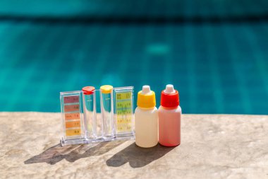 PH ve klor dereceli havuz suyu test kiti ve havuz kenarında reaksiyonlu şişeler, yüzme havuzu bakımı, su kalite kontrolü ve kimyasal denge kavramı. Yüksek kalite fotoğraf