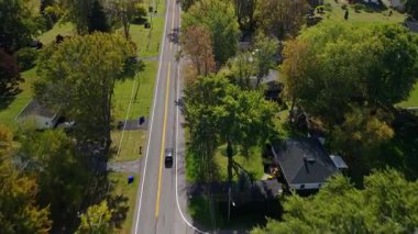 Sonbaharın başlarında sessiz Amerikan mahallesinde ağaçlar ve evlerle dolu düz banliyö yolunda giden bir arabanın hava manzarası. Yüksek kalite 4k görüntü