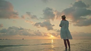 Gün batımında ve Lipa Noi plajında gün doğumunda çıplak ayakla sığ denizde yürüyen genç kadın, dramatik bulutlar ve geniş kopya alanı ile huzurlu tropikal seyahat sahnesi. Yüksek kalite 4k görüntü
