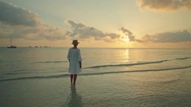 Gün batımında Lipa Noi plajında sığ denizde duran genç bir kadın, Koh Samui, geniş kopya alanı ve altın gökyüzü ile huzurlu bir tropikal seyahat anı. Yüksek kalite 4k görüntü