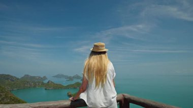 Hasır şapkalı genç kadın manzaralı bir bakış açısıyla, turkuaz deniz ve tropikal Ang Thong adaları üzerinde Tayland 'da huzurlu bir seyahat anı bekliyor. Yüksek kalite 4k