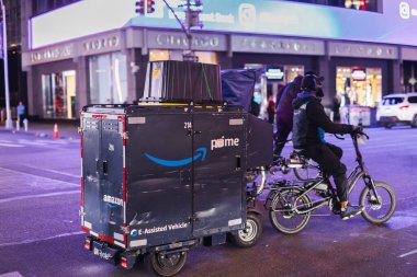 New York, ABD, 1 Kasım 2025: Amazon Prime dağıtım işçisi gece şehir sokaklarında elektrikli kargo bisikleti sürüyor şehir ışıkları ve modern lojistik ulaşımıyla