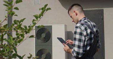 Teknisyen evin yakınındaki tableti kullanarak ısı pompası sistemini kontrol ediyor..
